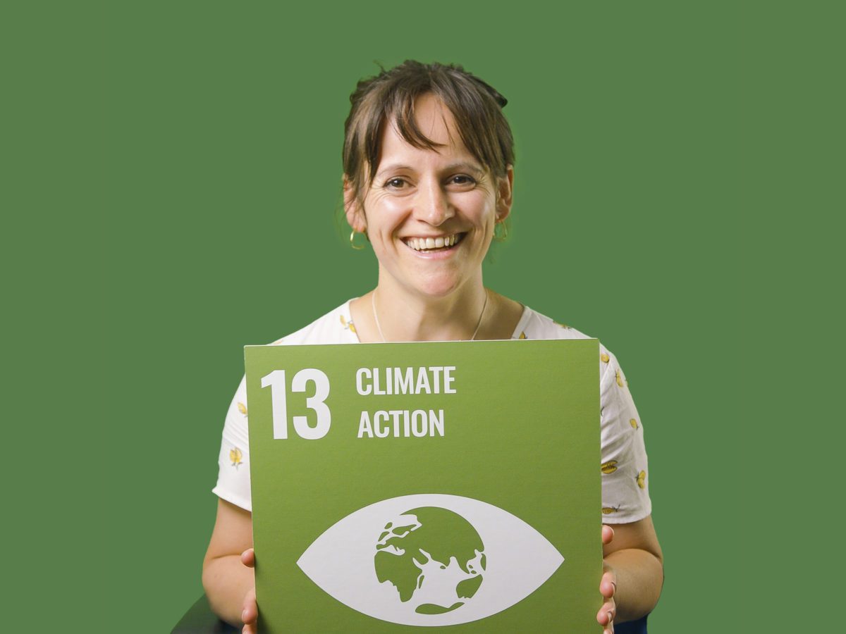 Woman holding up sign showing Global Sustainable Development Goal 13, climate action.