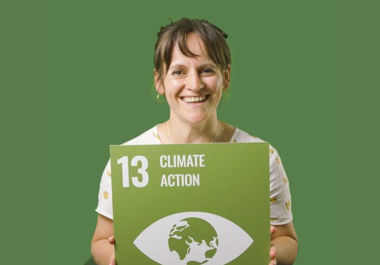 Woman holding up sign showing Global Sustainable Development Goal 13, climate action.