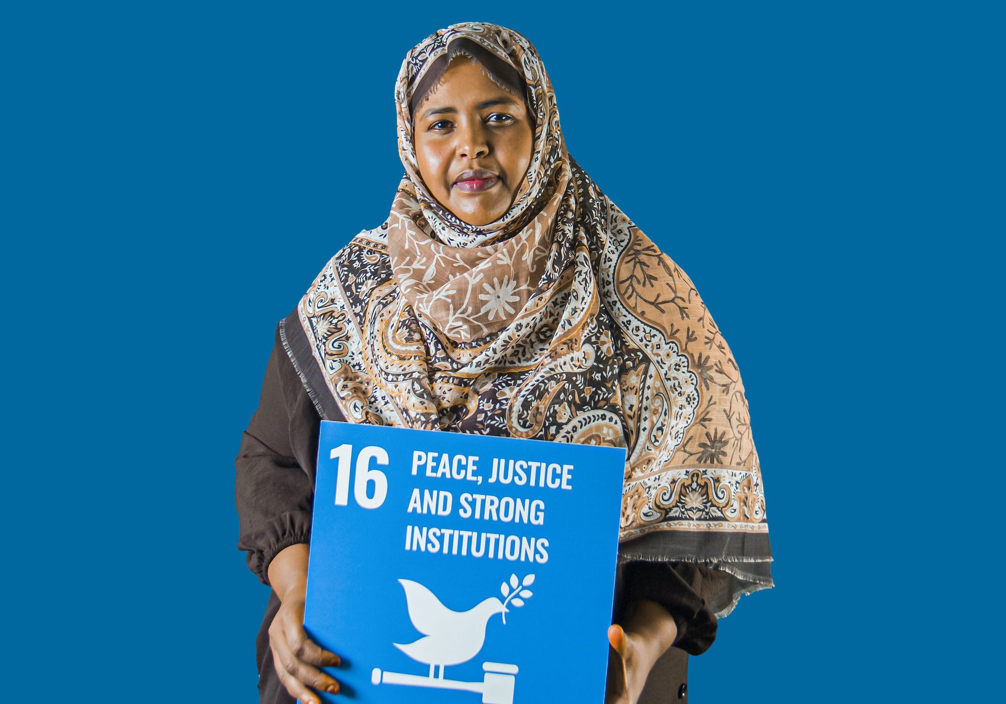 Woman holding up sign showing Global Sustainable Development Goal 16, peace, justice and strong institutions.