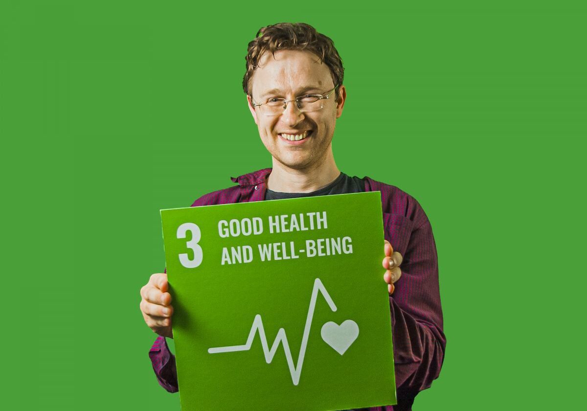 Man holding up sign showing Global Sustainable Development Goal 3, good health and well-being.